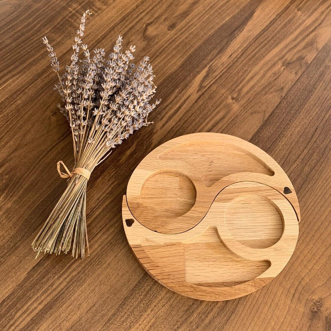 Round wood-tone serving tray with two curved sections beside dried flowers