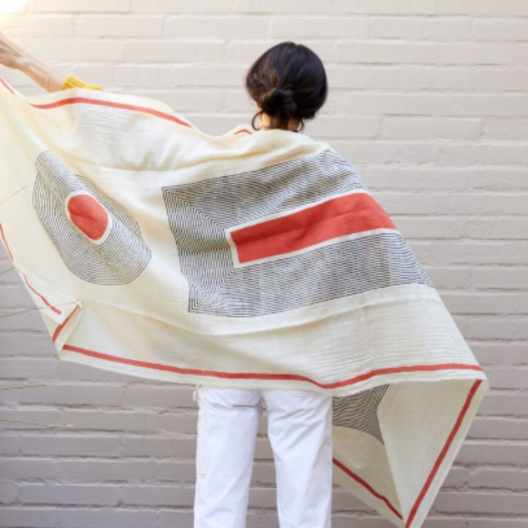 Model holding open a cream scarf with grey and red abstract shapes.