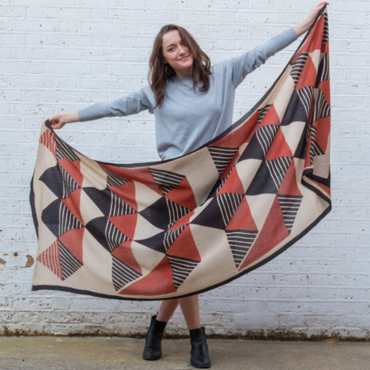 Model holding a red, black and cream geometric stole open to show its pattern.