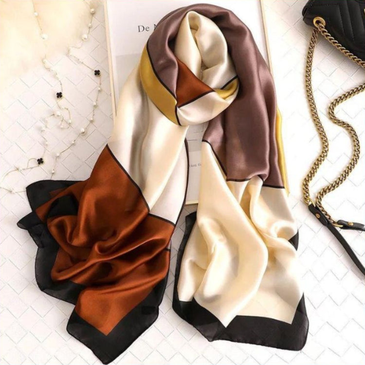Rust, cream and brown colour-block scarf draped on a hanger beside accessories.