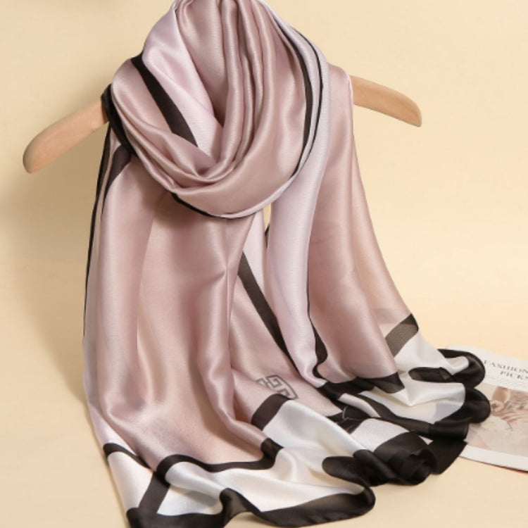 Blush pink scarf with black borders draped on a wooden hanger.