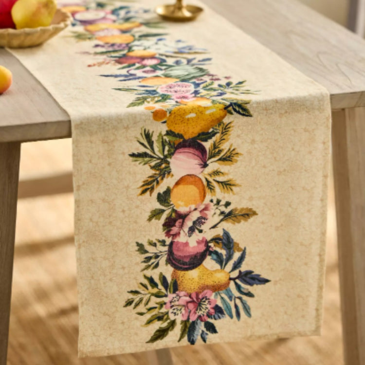 Beige table runner with a central arrangement of colourful flowers and fruit.