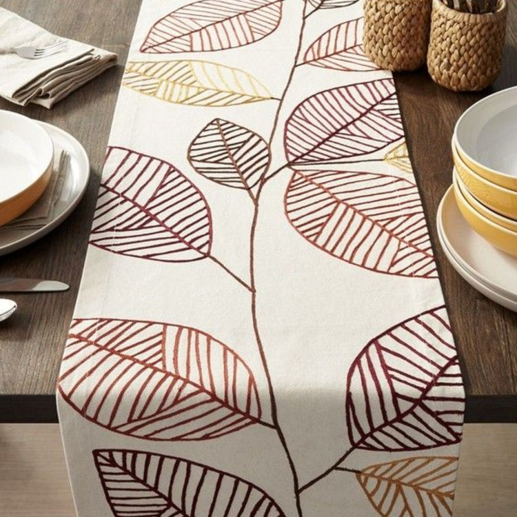 Cream table runner with large outlined brown and grey leaves.