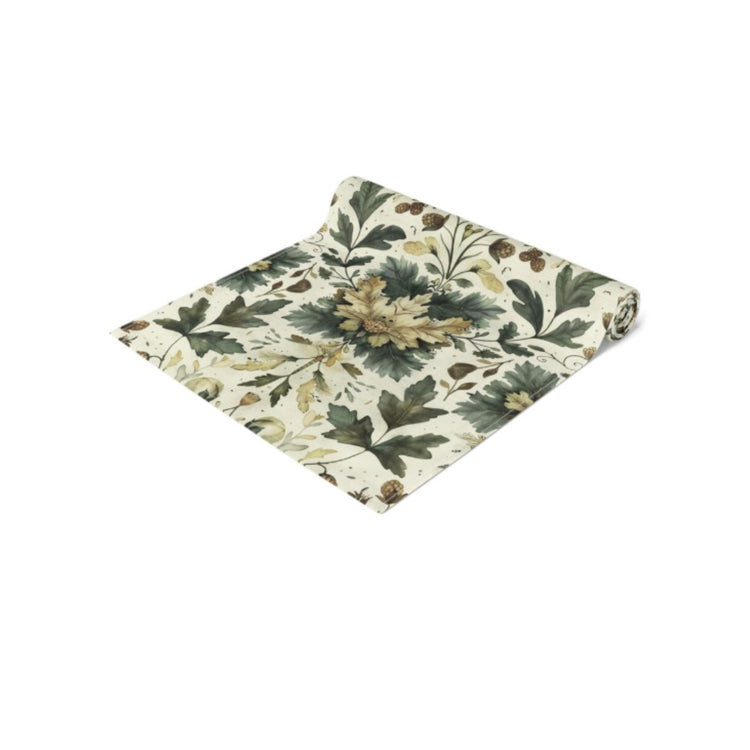 Folded cream table runner with green and gold botanical motifs.