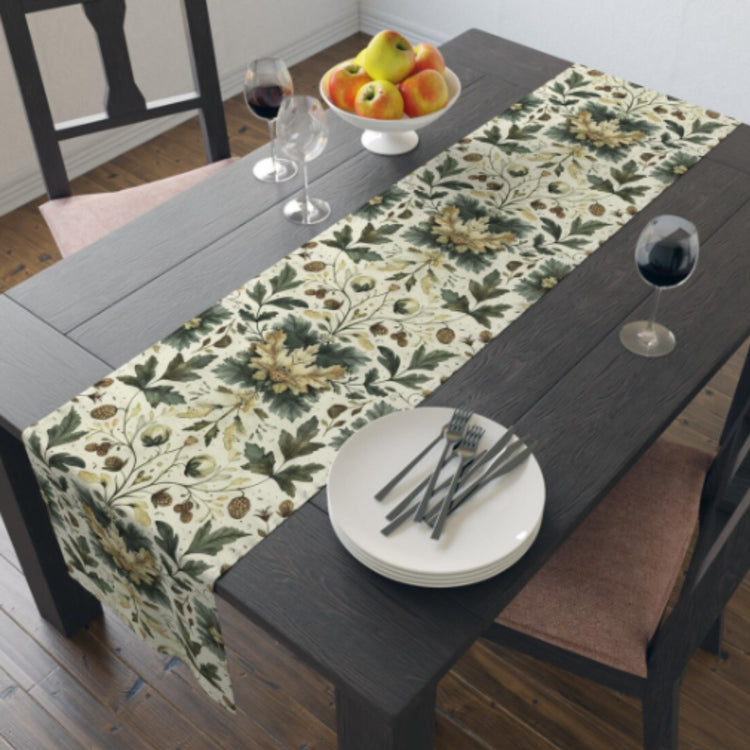Cream botanical table runner with green leaves and gold flowers beneath white plates.
