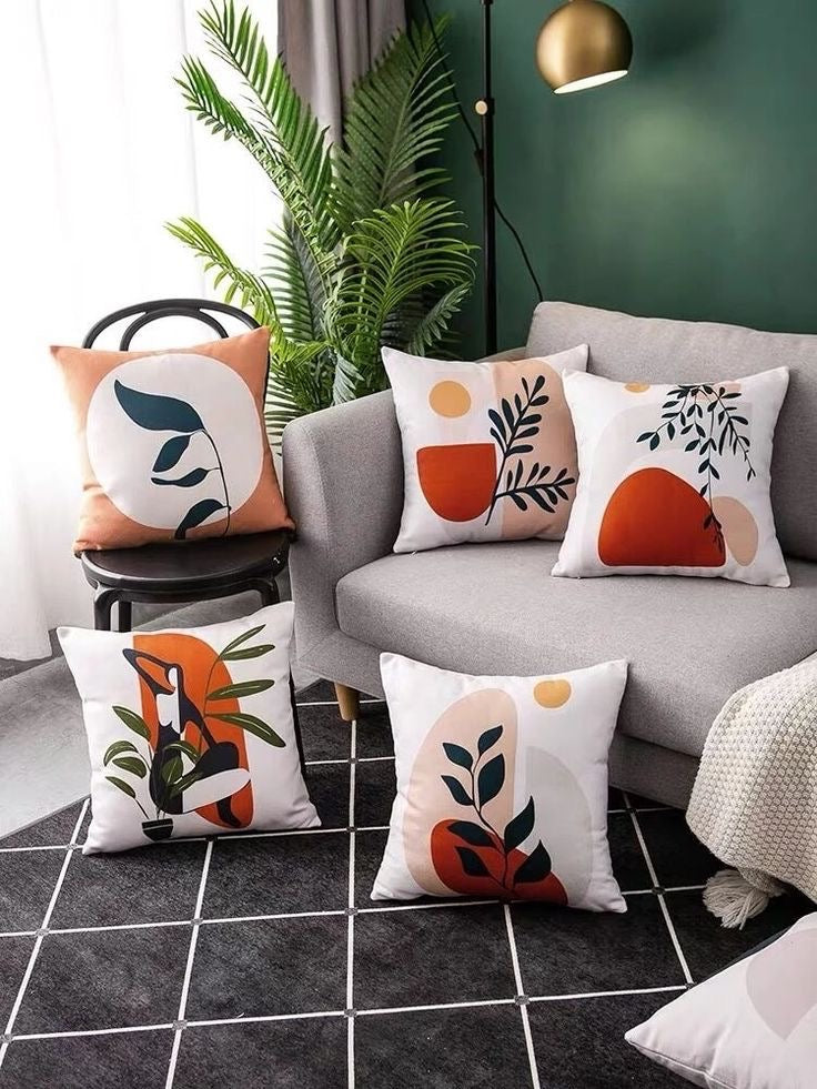 Five cushion covers with orange, green and black abstract botanical designs in a living room.