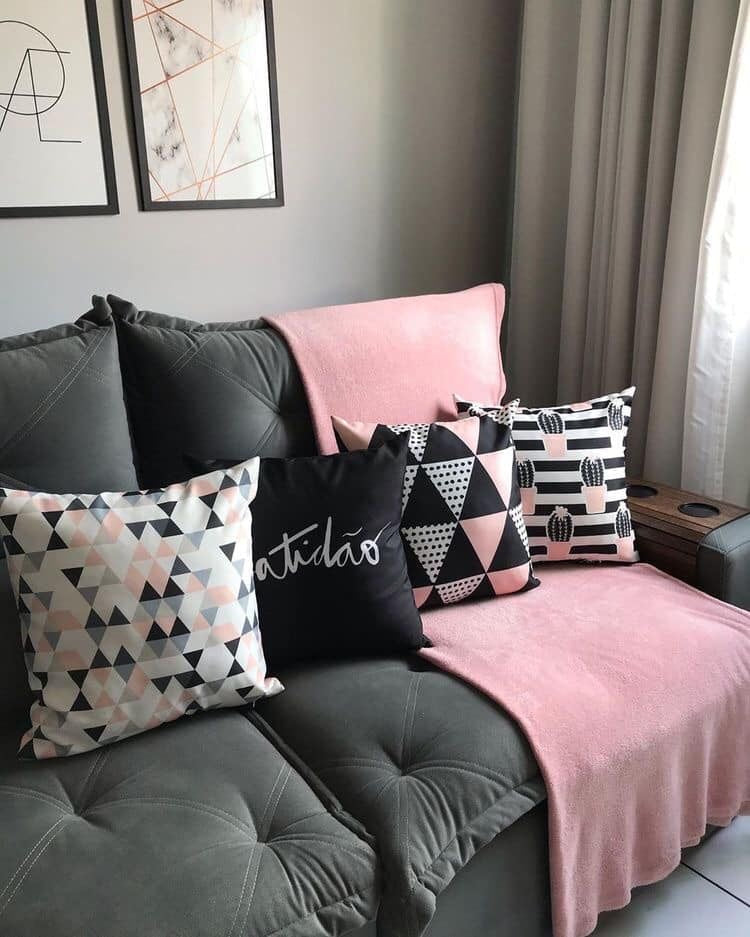 Pink, black and white plain and geometric cushion covers arranged on a dark sofa.