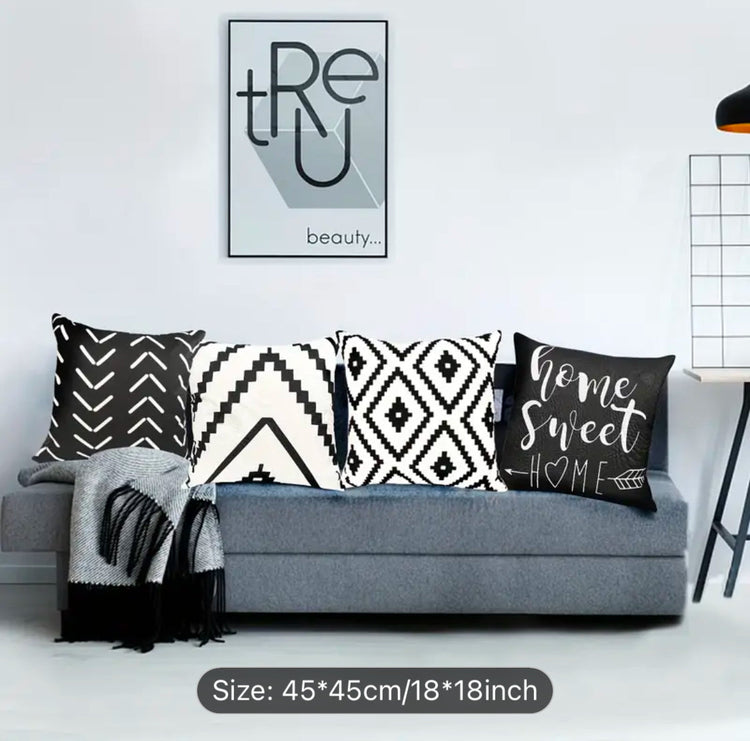 Four black and cream cushion covers with geometric patterns and Home Sweet Home lettering on a sofa.