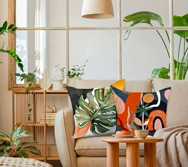 Green botanical and orange abstract cushion covers displayed together on a wooden chair.