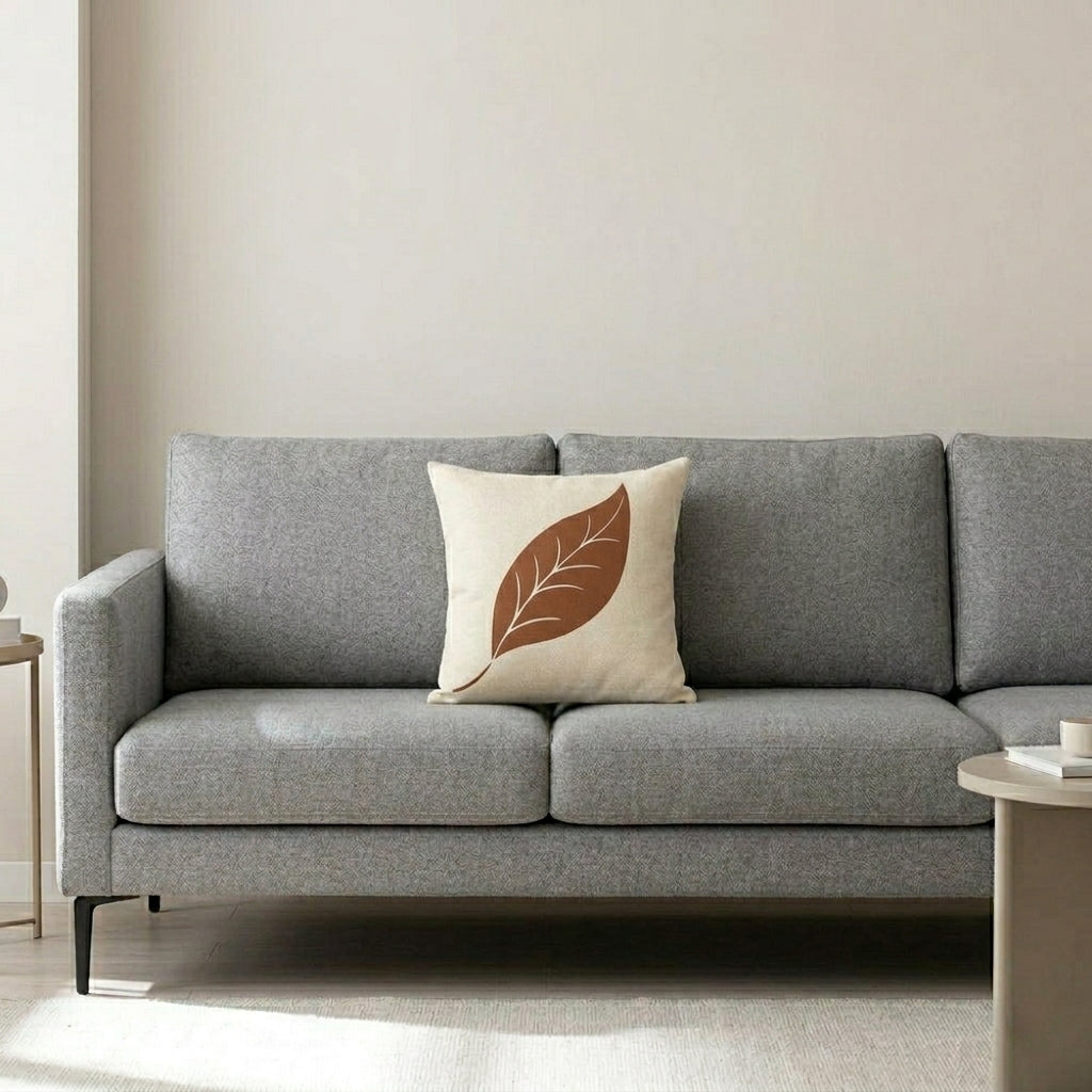Cream cushion cover with a single terracotta leaf on a grey sofa.