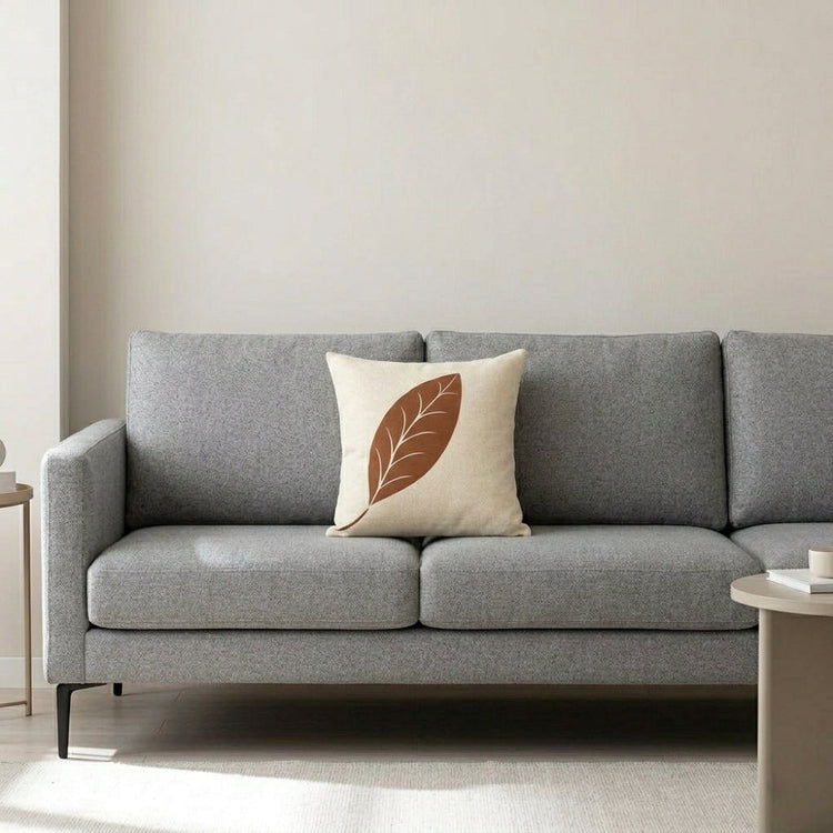 Cream cushion cover with a terracotta leaf and fine vein details on a grey sofa.
