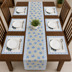 A dining table set with a blue and beige floral table runner down the center, matching placemats with white plates and silverware, and wooden chairs around it.