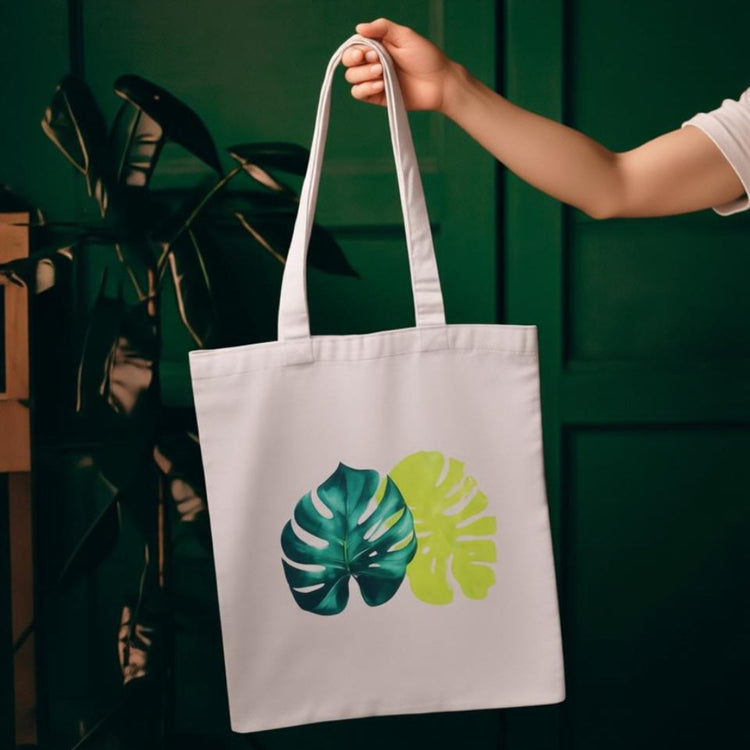 Cream tote bag with two overlapping green and yellow tropical leaves.