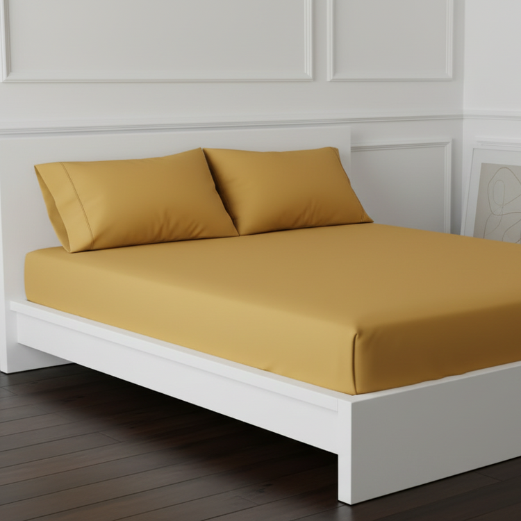 Ochre cotton fitted sheet displayed on a bed with matching pillowcases.