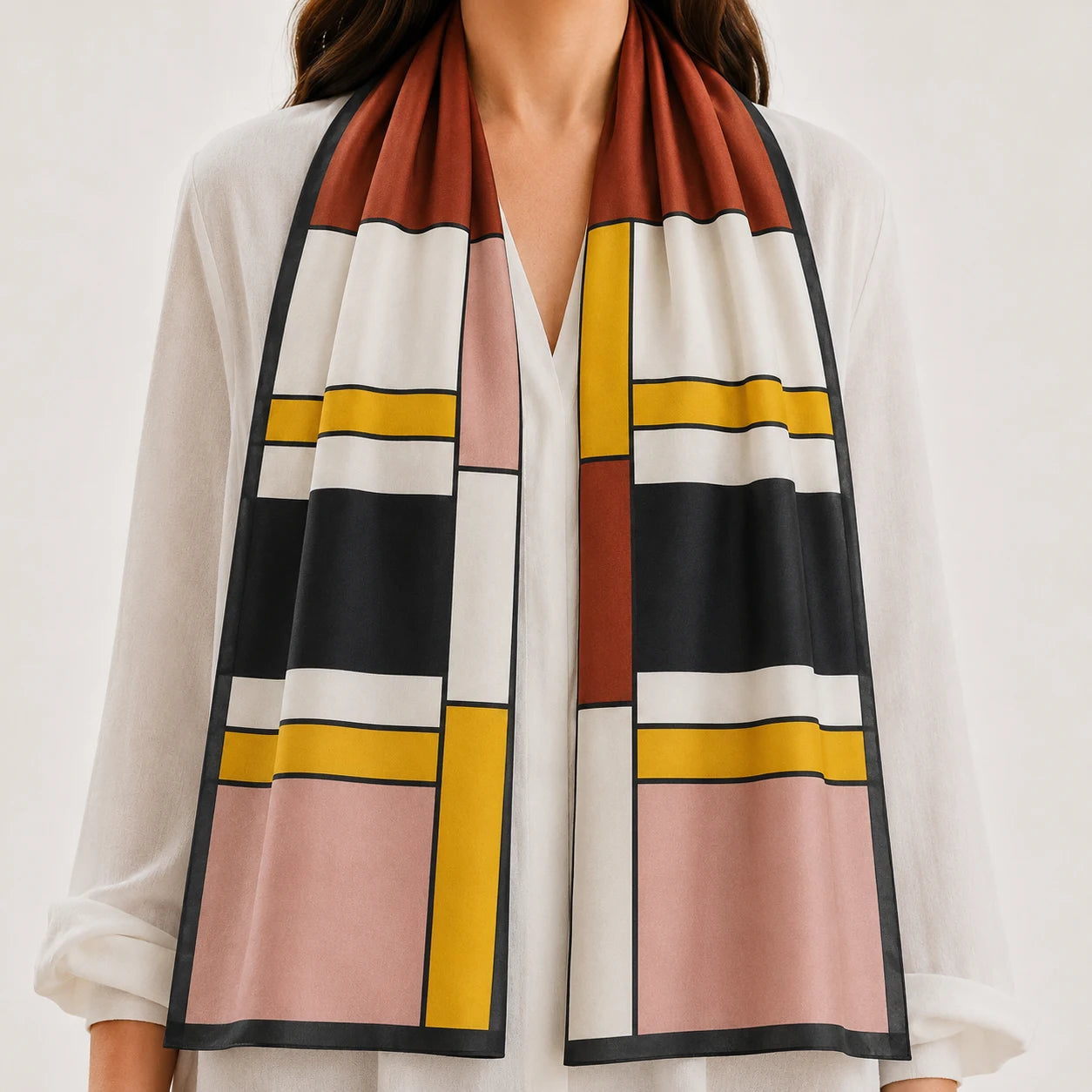 A woman wearing a white blouse and a long rectangular scarf with a geometric block pattern in rust brown, black, white, pink, and mustard yellow.