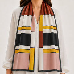 A woman wearing a white blouse and a long rectangular scarf with a geometric block pattern in rust brown, black, white, pink, and mustard yellow.