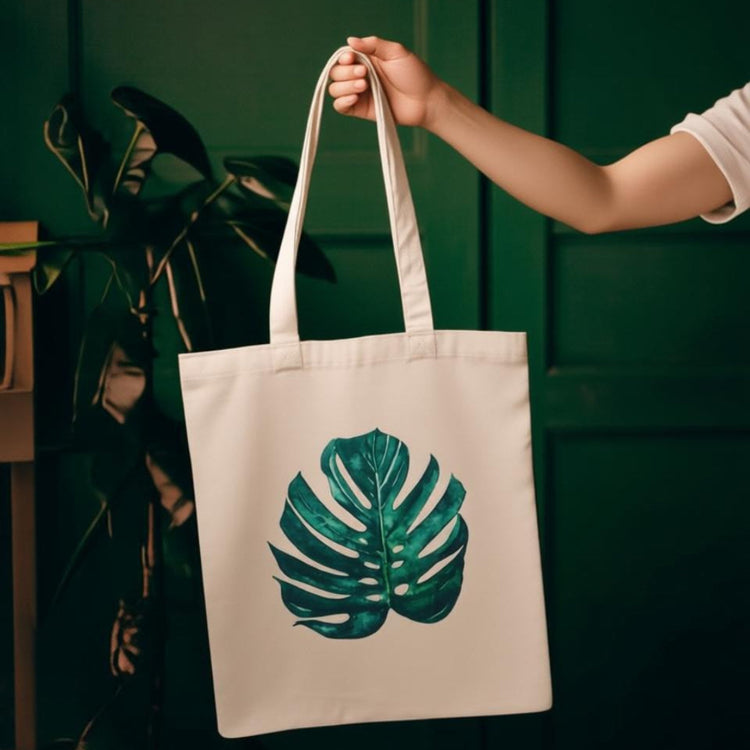 Cream tote bag with a single large dark green monstera leaf.