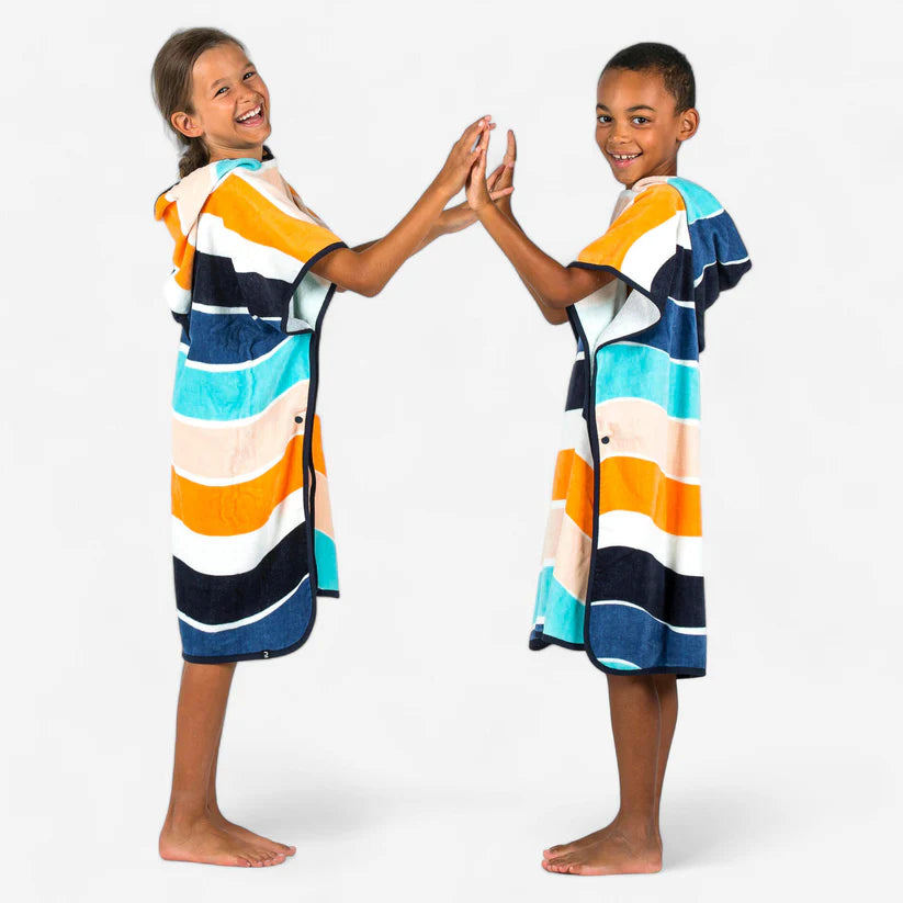 Two children wearing matching multicoloured striped towel ponchos.