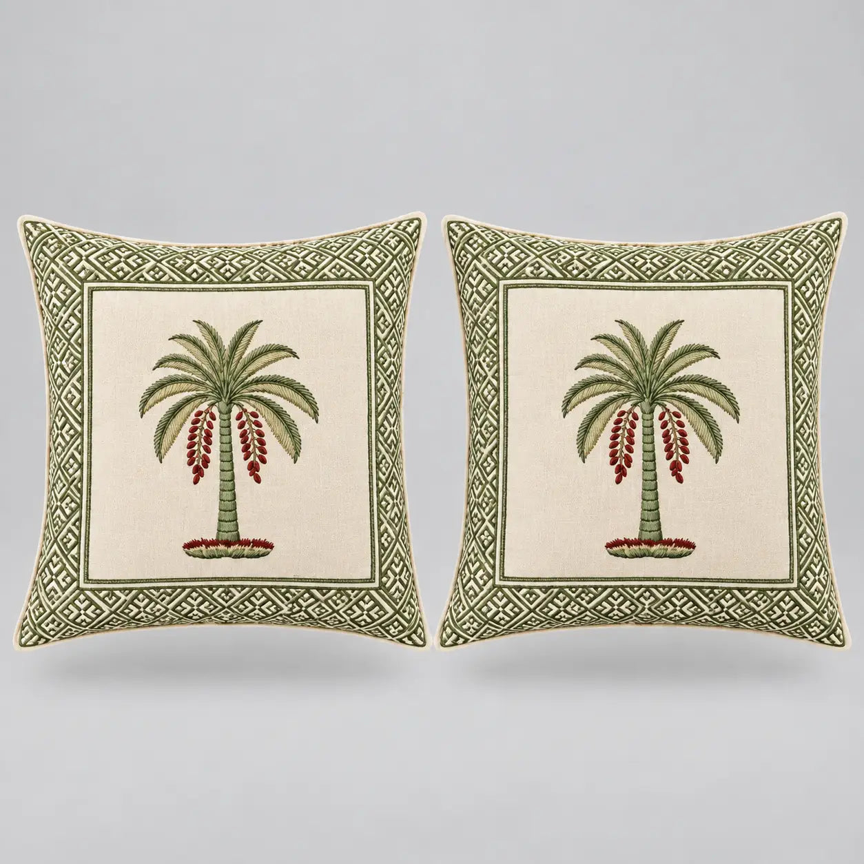 Two square decorative throw pillows shown side by side on a light gray background. Each pillow has an off-white center panel featuring a green palm tree with red hanging fruit, surrounded by a green geometric border.