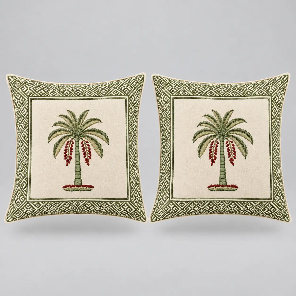 Two square decorative throw pillows shown side by side on a light gray background. Each pillow has an off-white center panel featuring a green palm tree with red hanging fruit, surrounded by a green geometric border.