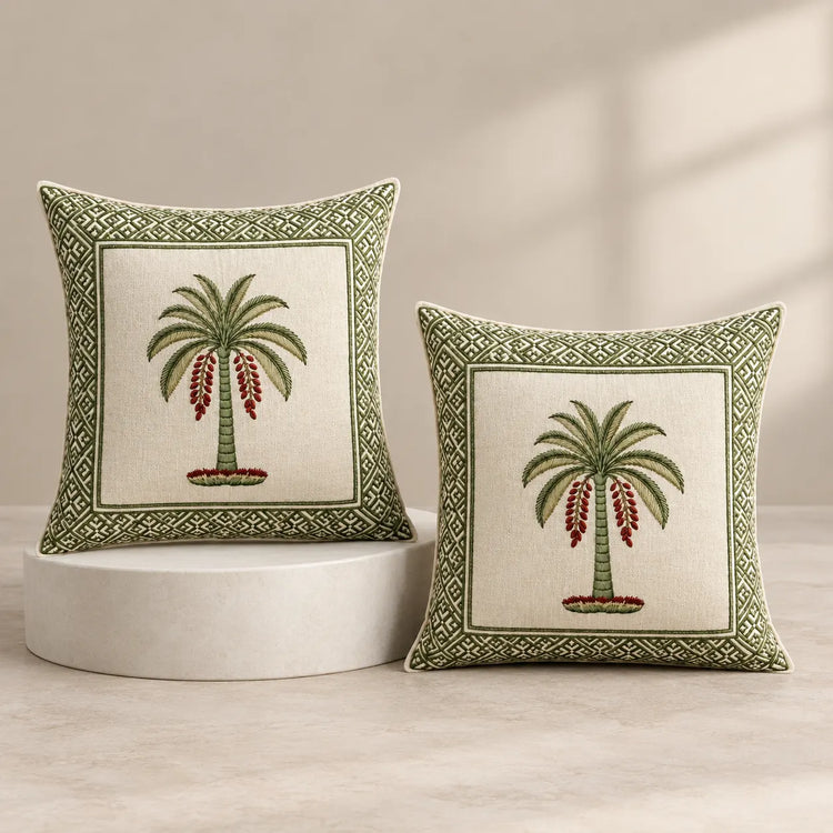 Two decorative throw pillows with embroidered palm tree designs and geometric borders, displayed on a light beige floor against a neutral wall with soft window-shadow lighting.