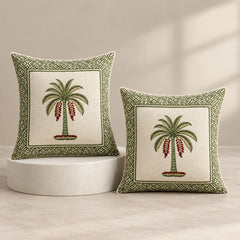 Two decorative throw pillows with embroidered palm tree designs and geometric borders, displayed on a light beige floor against a neutral wall with soft window-shadow lighting.