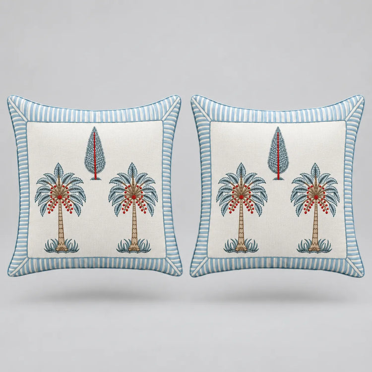 Two square decorative throw pillows with a light blue and white striped border, featuring a central cream-colored panel with embroidered palm trees and a small tree motif.