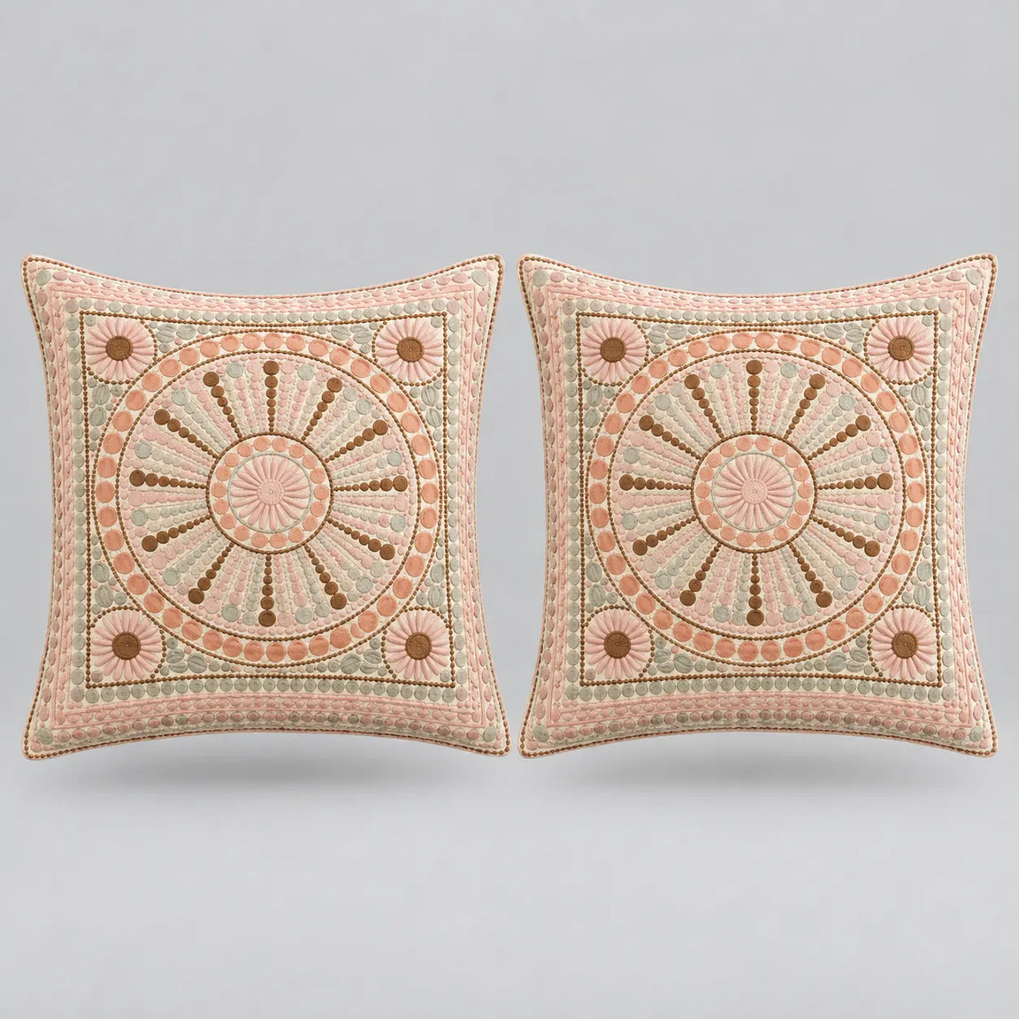 Two square decorative throw pillows with intricate circular medallion embroidery in dusty pink, beige, and brown, set against a solid light gray background.