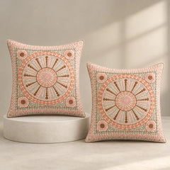Two square decorative throw pillows with intricate circular mandala embroidery in peach, brown, and sage green, displayed on a light gray pedestal and a neutral beige background.