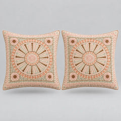 Two square decorative throw pillows with intricate circular medallion embroidery in dusty pink, beige, and brown, set against a solid light gray background.