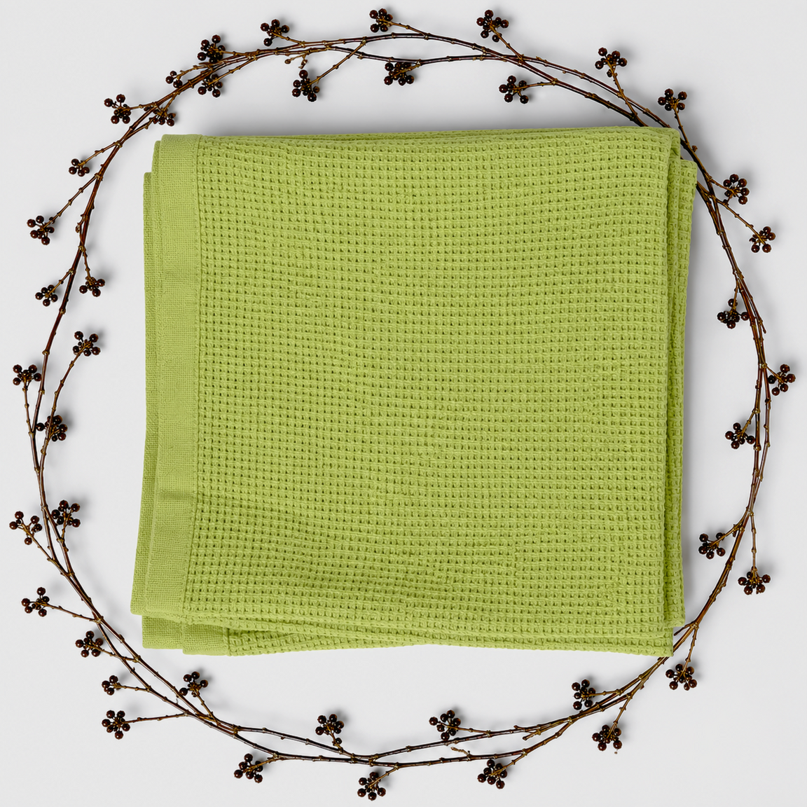 Folded light green baby blanket with a waffle texture and plain border, surrounded by decorative berry branches.