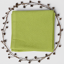 Folded light green baby blanket with a waffle texture and plain border, surrounded by decorative berry branches.