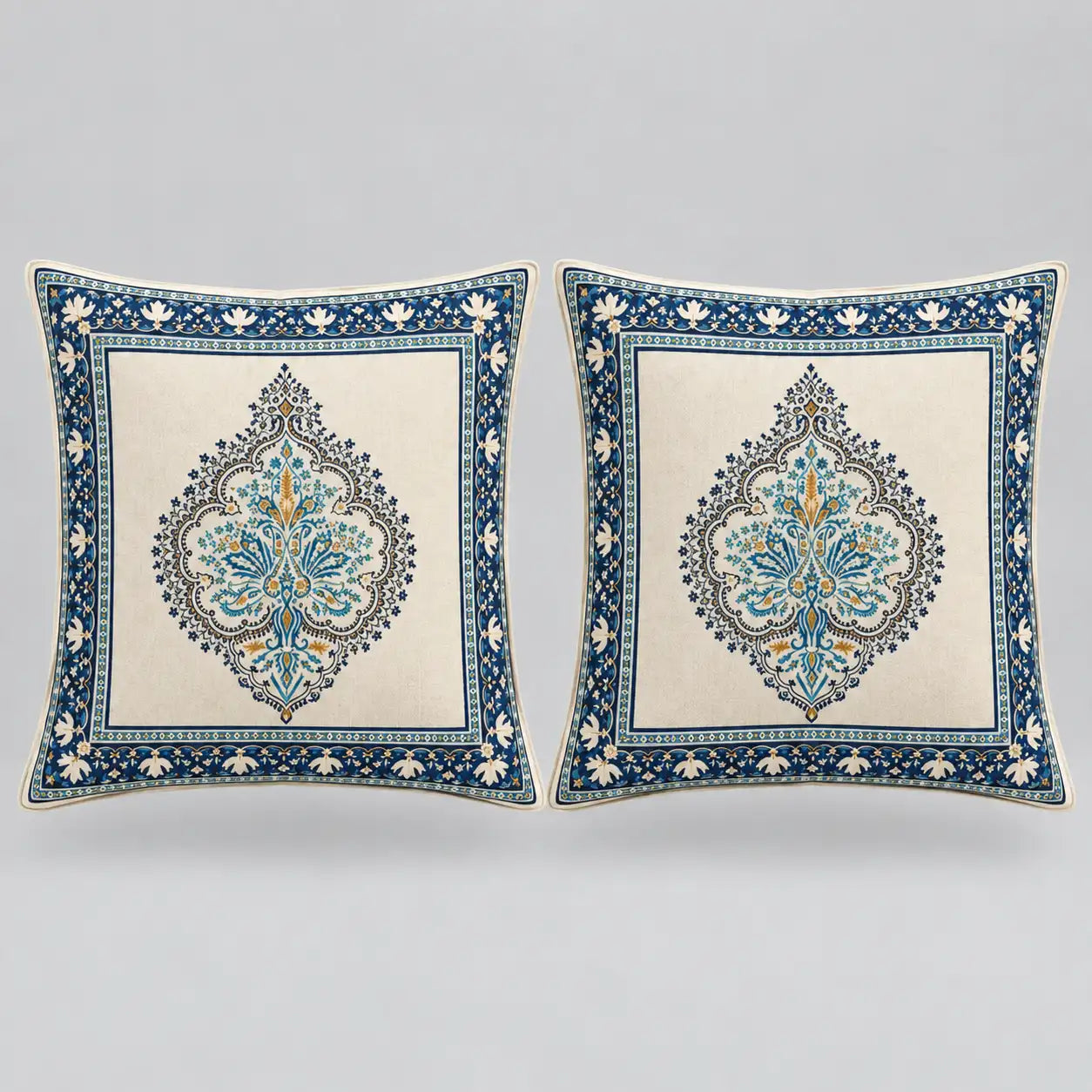 Two square decorative throw pillows with intricate blue and gold traditional patterns on a cream background, set against a neutral gray studio backdrop.