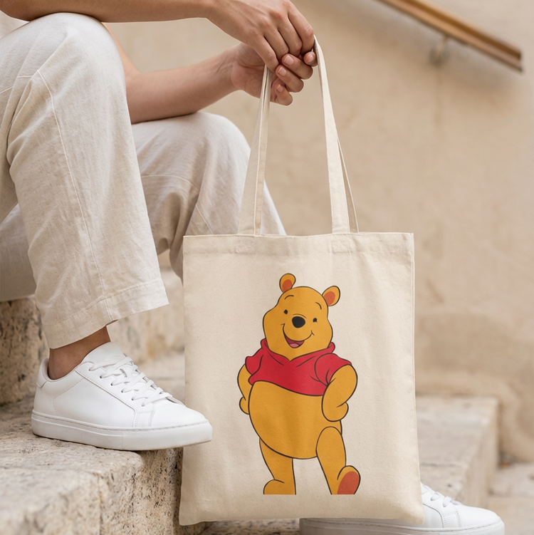 Cream tote bag with a yellow cartoon bear wearing a red shirt.