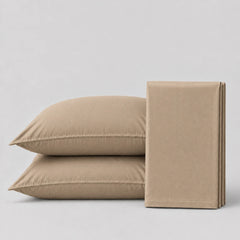 Light tan  bedsheet and pillows  on a light grey surface 