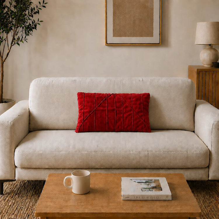 Rectangular red filled cushion with angular stitched lines on a cream sofa.