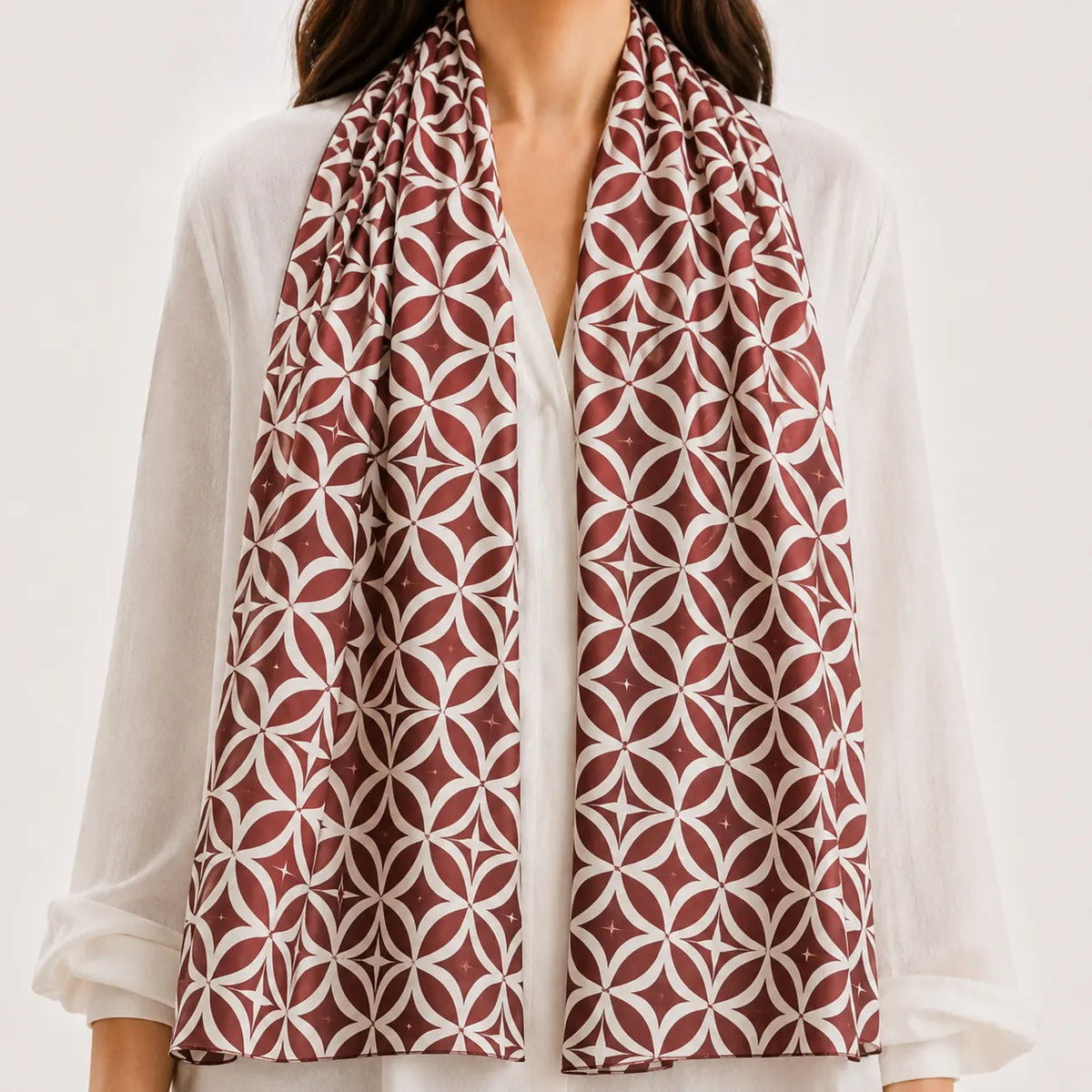 A woman wearing a white  and a long patterned scarf in rust red and white with a geometric interlocking circle design.