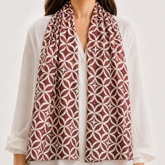 A woman wearing a white  and a long patterned scarf in rust red and white with a geometric interlocking circle design.