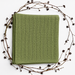 Folded sage green baby blanket with narrow vertical textured stripes and a plain border.