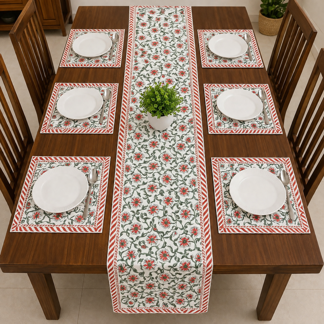 A rectangular wooden dining table set for six with a floral table runner and matching placemats. The placemats and runner feature a red and green floral pattern on a white background with red-and-white striped borders.
