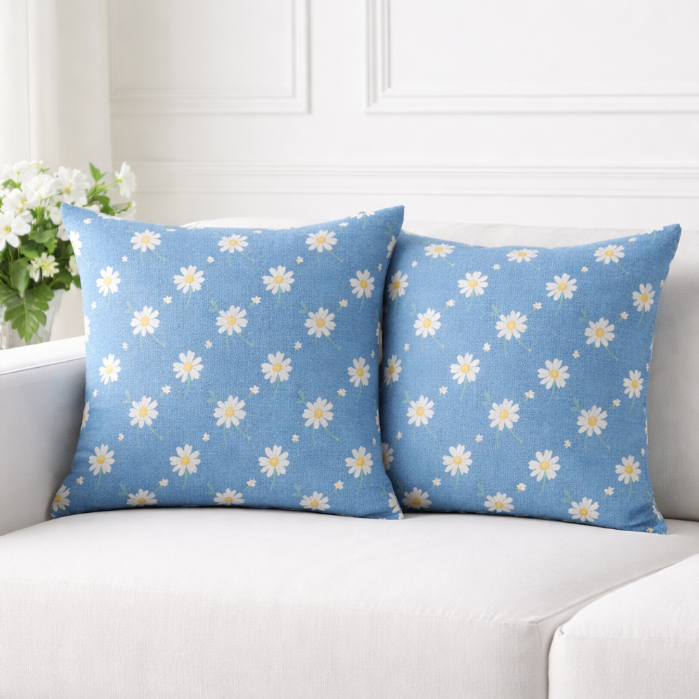 Two blue cushion covers with small scattered white daisies on a sofa.