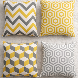Four yellow, grey and white cushion covers with zigzag, cube and hexagon patterns.