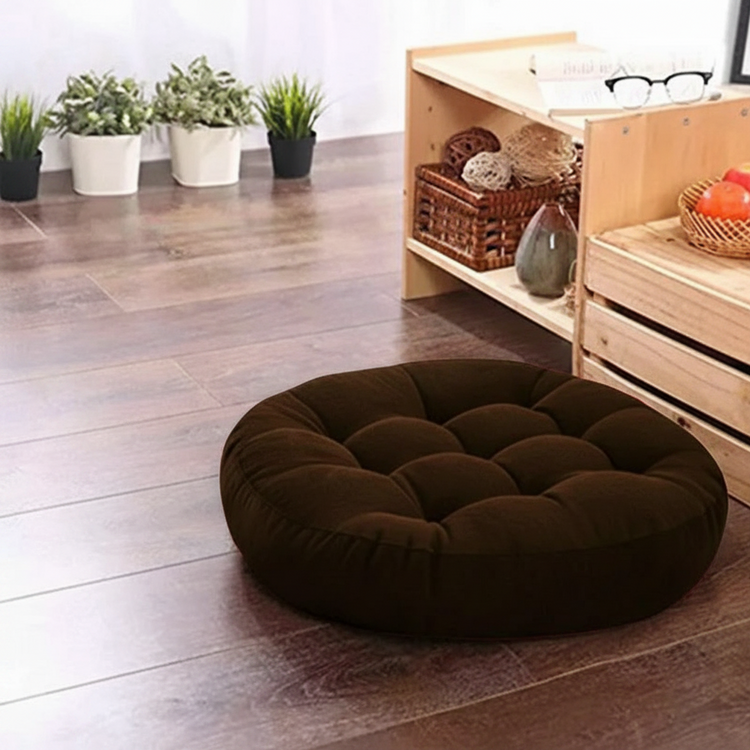 Round dark brown tufted floor cushion on a wooden floor.