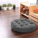 Round grey tufted floor cushion on a wooden floor.