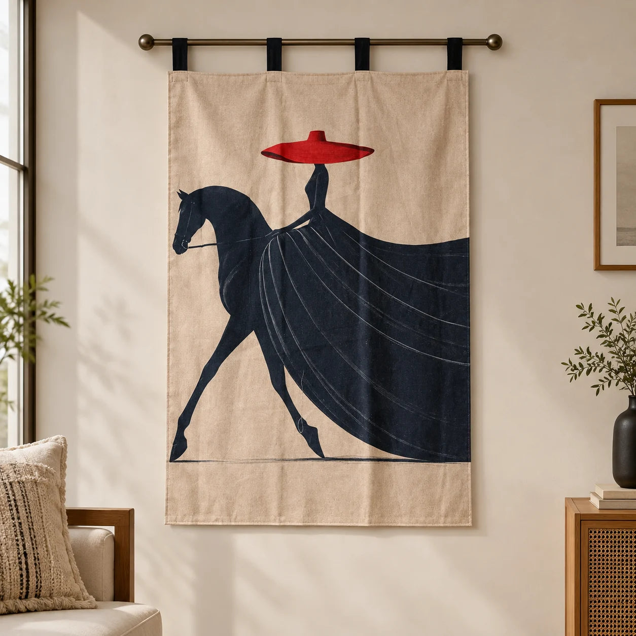A beige wall hanging or tapestry with a stylized dark navy horse and rider graphic and a bright red hat, suspended from a metal rod in a softly lit room.
