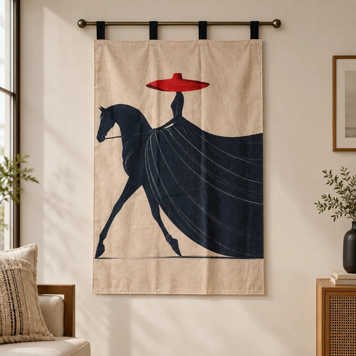 A beige wall hanging or tapestry with a stylized dark navy horse and rider graphic and a bright red hat, suspended from a metal rod in a softly lit room.
