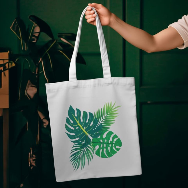 Cream tote bag with a cluster of green tropical leaves.