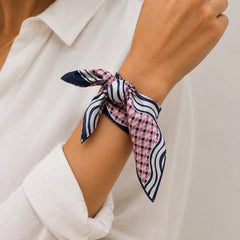 A close-up of a person's wrist wearing a small patterned silk scarf tied in a knot, paired with a white button-down shirt.