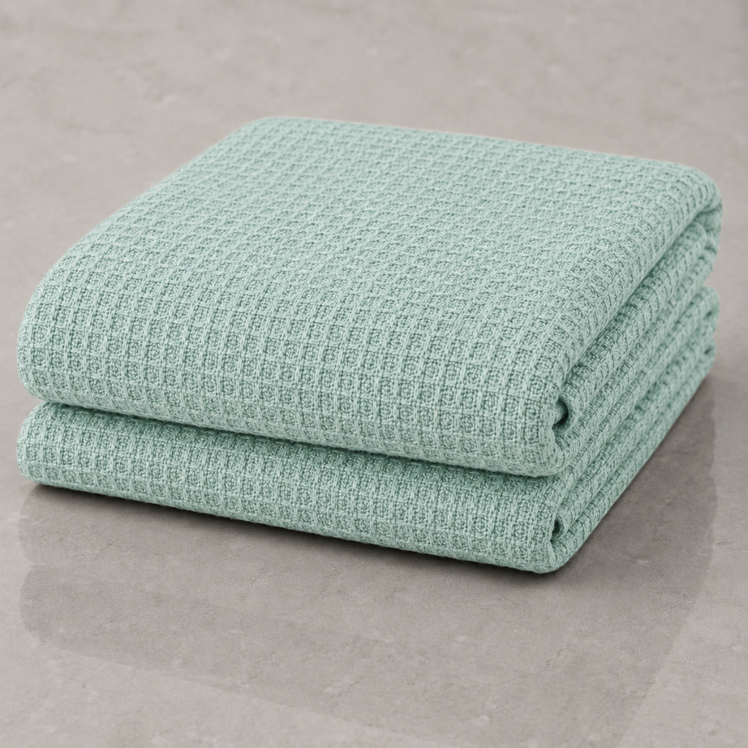 Two folded waffle-weave towels in a light mint green color, stacked on a neutral gray surface.