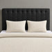 A neatly made bed with a textured cream waffle blanket, two matching cream pillows, and a tall black tufted headboard against a gray wall.